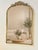 A gilt metal mirror from the 2000s. Its arched shape is topped by a tall pediment decorated with scrolls and floral...