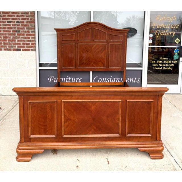 This queen-size bed frame features a warm cherry finish and a classic paneled design highlighted by raised moldings and a...