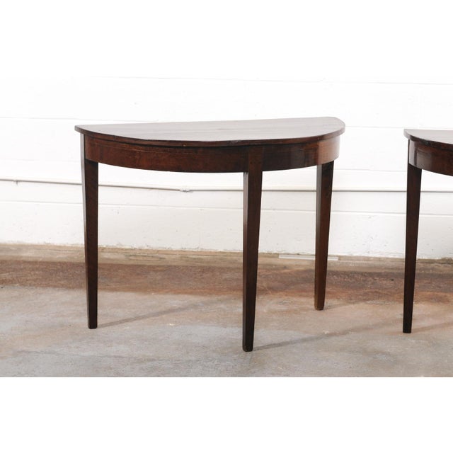 An Italian pair of wooden demi-lune console tables from the 19th century. These antique tables from Italy, embodying the...