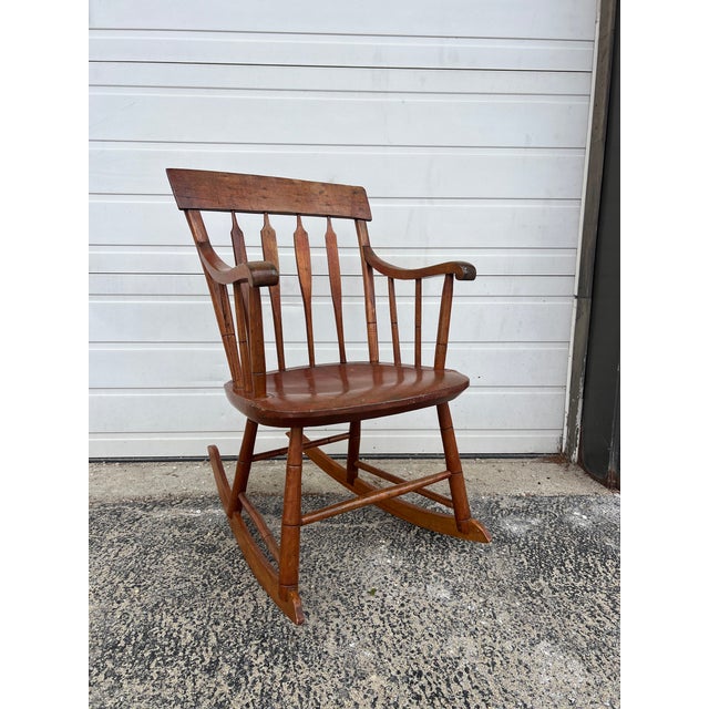 This antique petite rocking chair features hardwood construction, original maple finish, sculpted wood arms, turned frame...