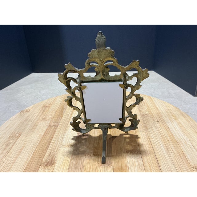 An ornate vintage tabletop picture frame cast in solid brass, designed in the classic Rococo / Baroque Revival style. The...