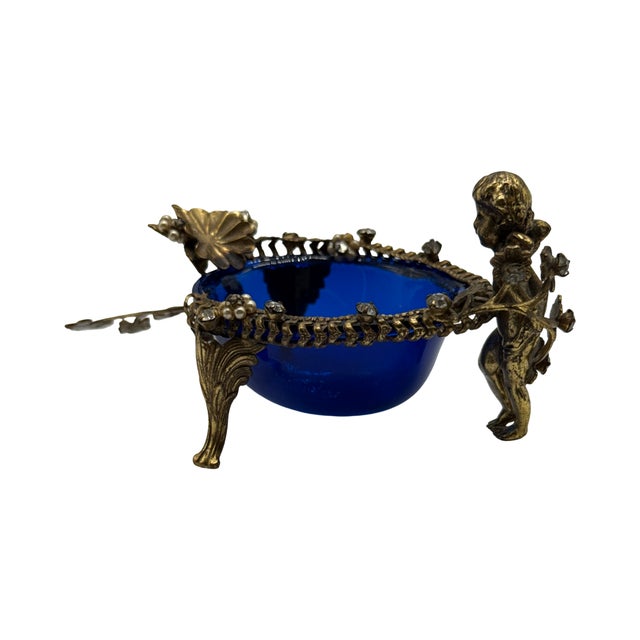 A charming antique cherub vanity dish featuring a cobalt blue hand-blown glass insert within an ornate gilt metal mount...