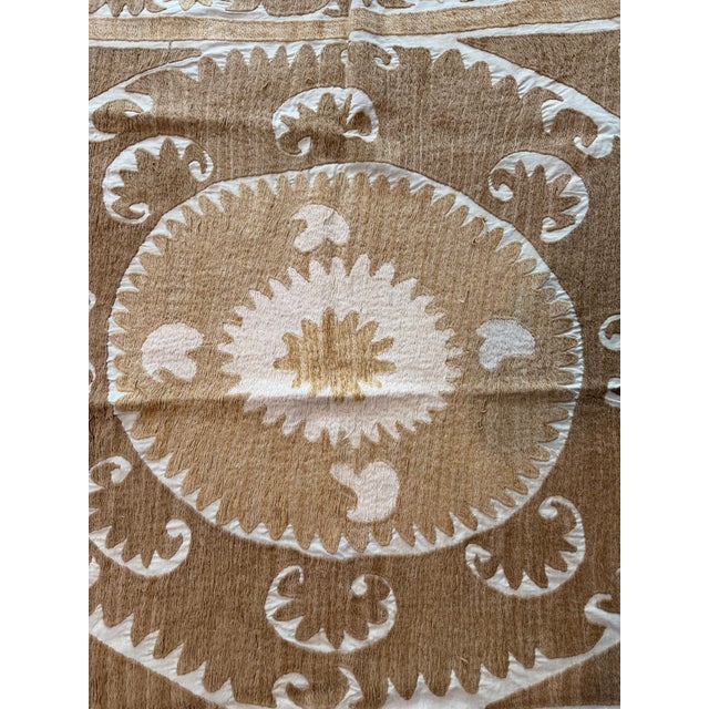 Hand-embroidered Suzani panel from Uzbekistan — a large tonal medallion in tan and ecru with curling leaf scrolls on an...