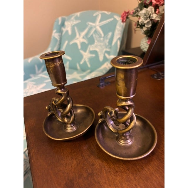 Striking pair of vintage brass candlesticks featuring a twisted column wrapped with a stylized serpent motif. The...