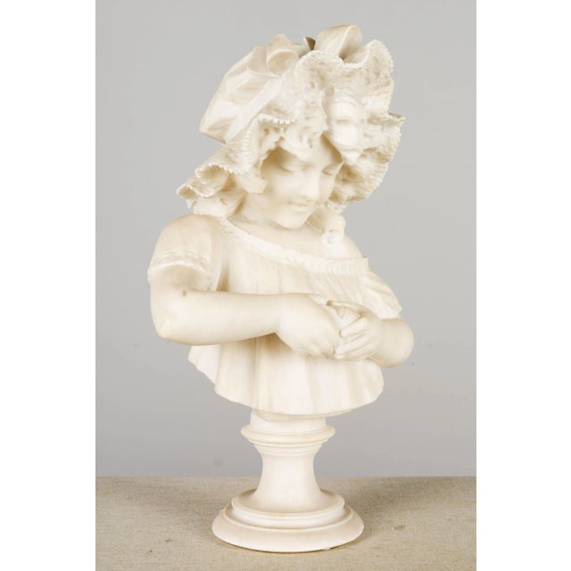 A 19th Century Italian alabaster bust of a young girl with a frilled bonnet peeling a orange. After a work by Italian...