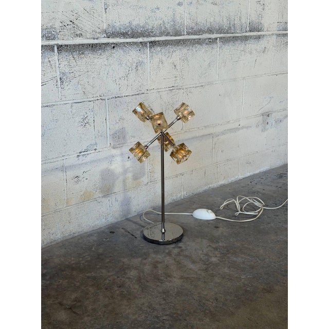 Geometric glass shades radiate from a slender chrome stem in a striking atomic configuration. Six sculptural cube lights...