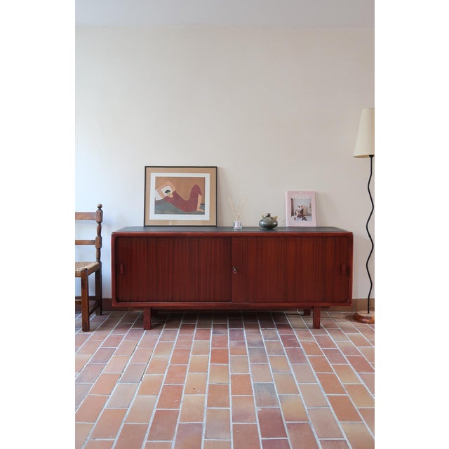 A 1970s teak sideboard with a low, quiet line: softly rounded corners, two sliding doors whose handles are hollowed...