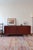 A 1970s teak sideboard with a low, quiet line: softly rounded corners, two sliding doors whose handles are hollowed...