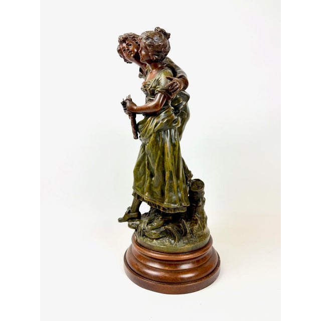 The sculpture depicts a young couple in period attire, captured in a joyful, dynamic motion. These figures embody...