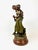 The sculpture depicts a young couple in period attire, captured in a joyful, dynamic motion. These figures embody...