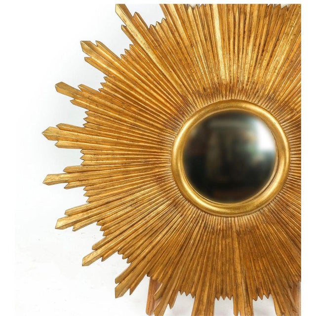 Gilt starburst mirror featuring a radiant, sculptural design with a round convex center mirror. Finished in a warm gilt...