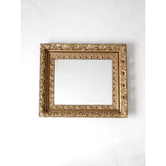 This antique gilt mirror features a rectangular frame adorned with richly detailed floral and scrollwork relief, finished...