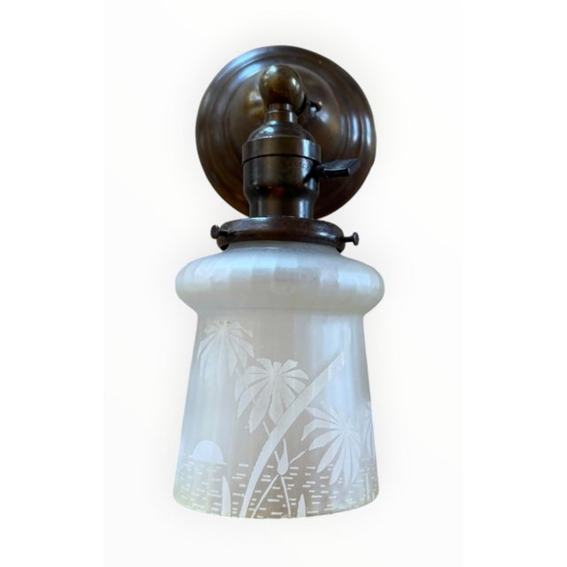This vintage brass wall sconce has an antique bronze patina and a frosted glass shade etched with a tropical palm tree...