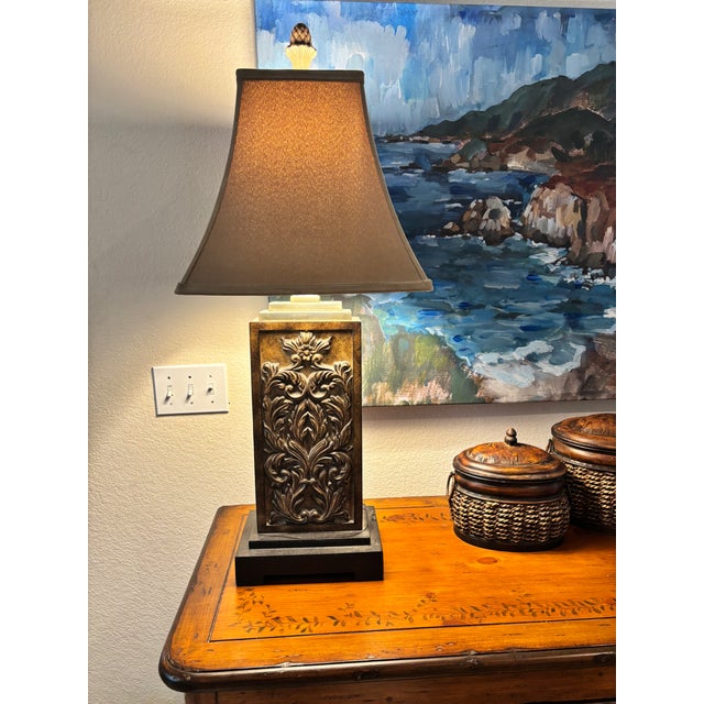 A striking vintage table lamp featuring a richly detailed acanthus leaf relief panel set within a substantial rectangular...