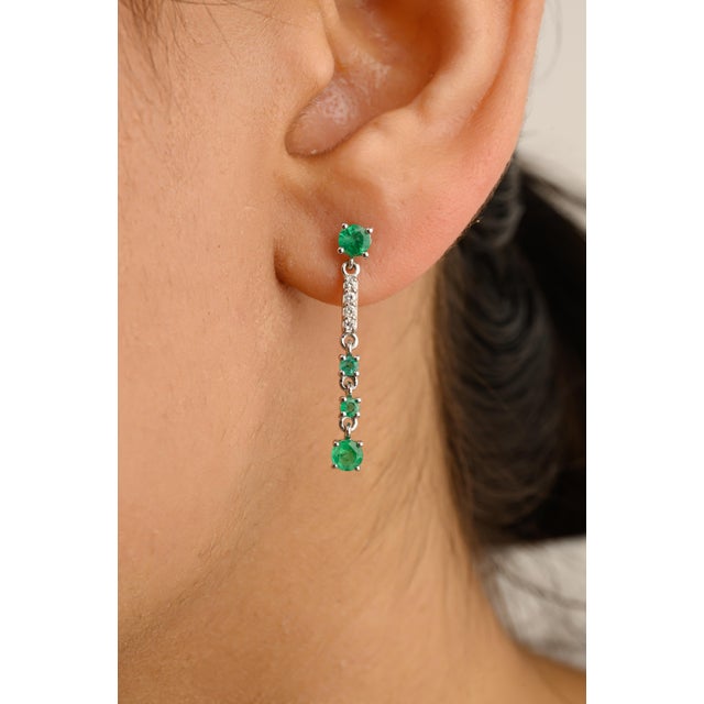 These elegant long dangle earrings feature vivid emeralds complemented by sparkling diamonds, creating a luxurious cascade...