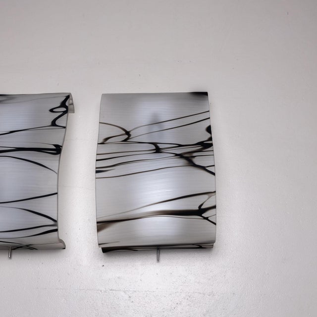 Pair of wall sconces featuring wavy glass shades crafted from white smoked glass with subtle black inclusions. The shades...