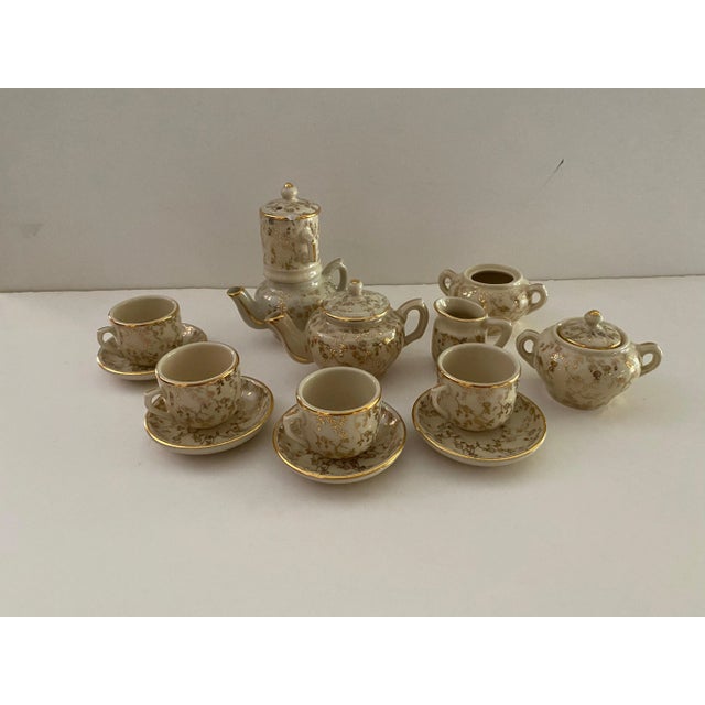 This Childs Tea set has a raised gold design and gold rims, It is 17 pieces. Two Coffee/tea pots, strainer, creamer, two...