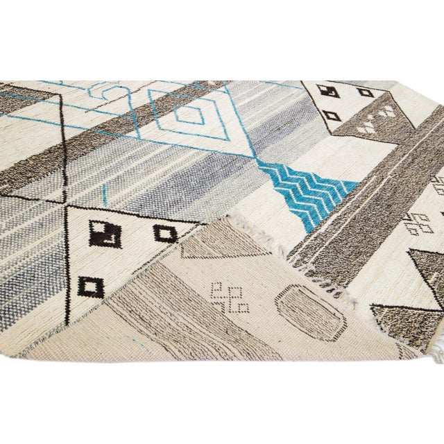 Beautiful modern Moroccan style hand-knotted wool rug with a beige field. This piece has gray, brown, and blue accent...