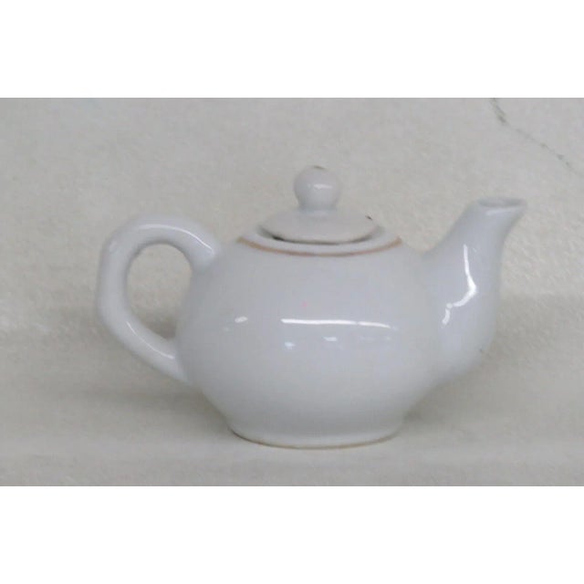 This charming miniature teapot is made of porcelain. This piece is stamped as being made in China, and it features a...