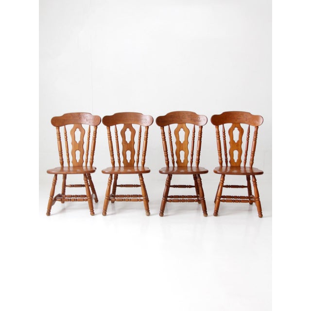A set of four vintage dining chairs in the Early American taste, featuring turned spindle backs, shaped crest rails,...