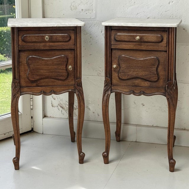 A fine pair of French Louis XV style antique nightstands crafted in oak and topped with beautifully shaped Carrara marble....