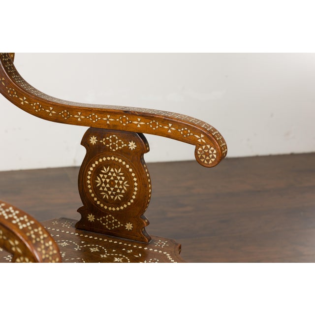 A Moorish style Moroccan wooden armchair from circa 1900 with bone inlaid décor, carved back, scrolling arms and carved...