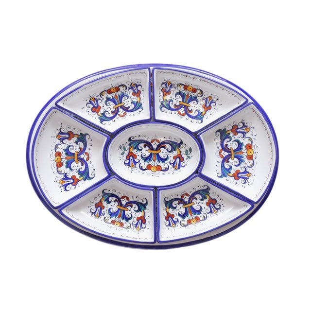 An Italian ceramic appetizer serving tray by Deruta. A large oval tray holds seven smaller trays, all hand painted in the...