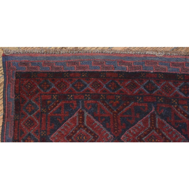A hand-knotted and woven Baluch tribal runner. This geometric wool rug is rendered in a palette of red, burgundy, and...