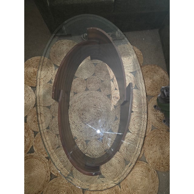 Good condition center coffee table. Oval glass top, with a unique design, warm/deep brown wood base, and small silver...