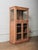 This vintage wooden display cabinet features a tall, narrow form with glass-paneled doors on multiple sides, allowing for...