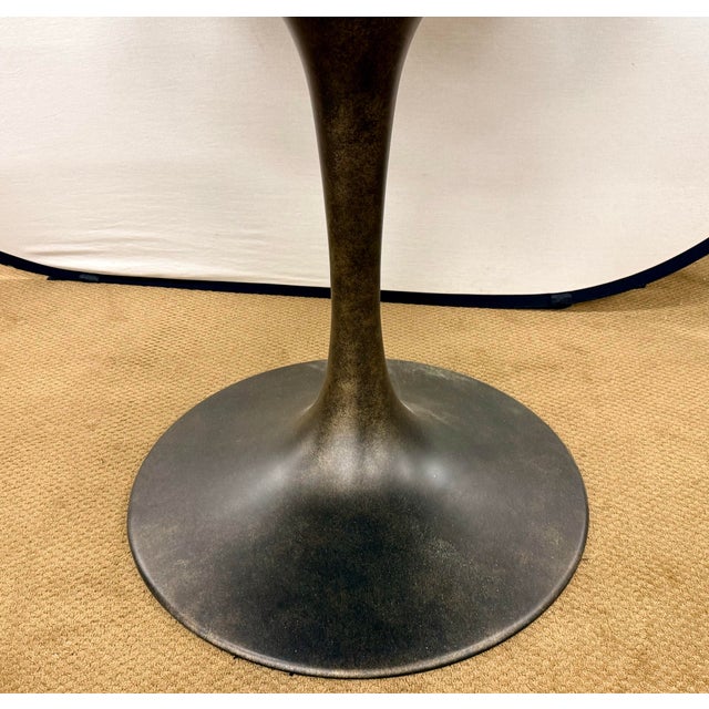 Williams Sonoma round tulip table with a black stone top and sculptural metal pedestal base with a bronze finish. A sleek,...