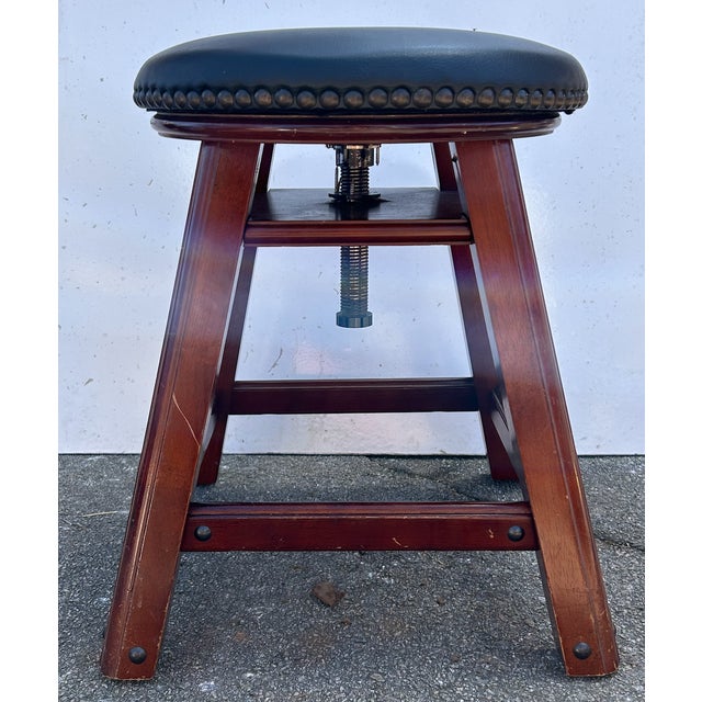 Description: Vintage adjustable piano stool featuring a solid wood frame, black leather upholstered swivel seat,...