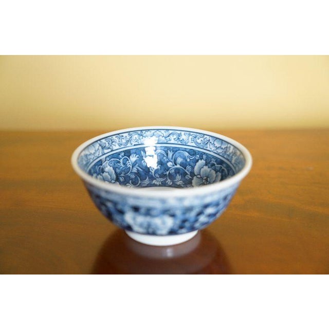 A small Chinese blue-and-white porcelain bowl featuring dense floral scroll decoration in deep cobalt blue against a white...