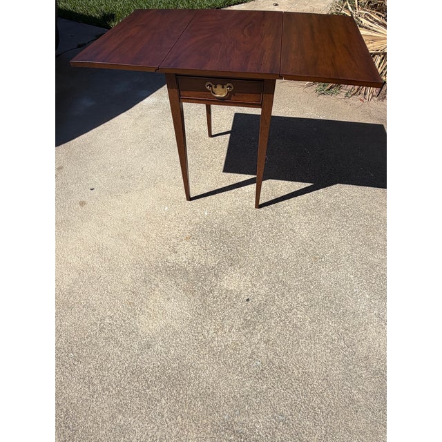 Rich mahogany grain, graceful tapered legs, and classic brass-tone hardware give this Henkel-Harris Pembroke table an...