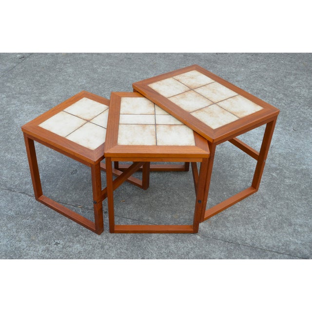 A great vintage set of 3 Danish Modern nesting tables in teak with inlaid tile tops. This matched nest of 3 solid wood...