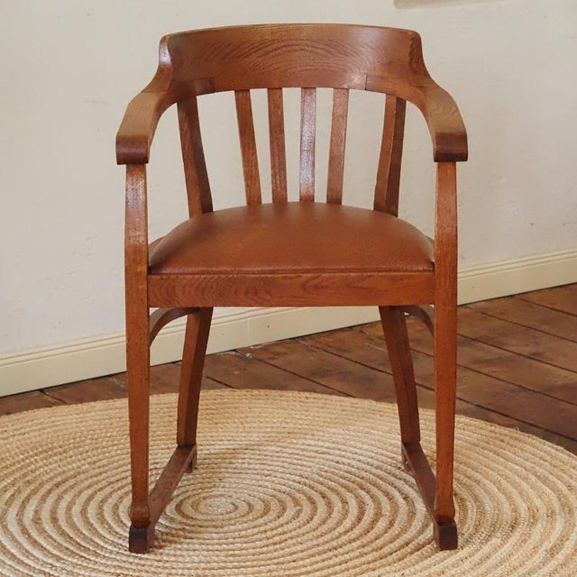 A semi-circular oak armchair, created around 1920–1930, reflecting the functional office and work furniture of the...