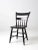 An antique primitive chair featuring a painted black plank seat, a half-spindle back, and splayed legs. Its understated...