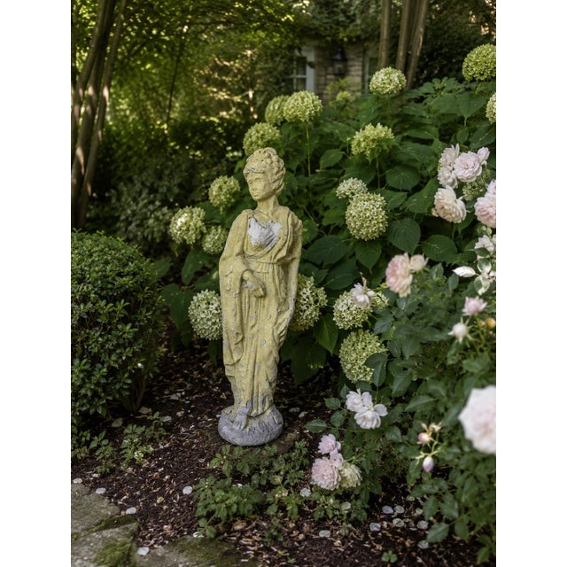 An evocative early-20th-century garden statue depicting a classically draped female figure in the Greco-Roman tradition....