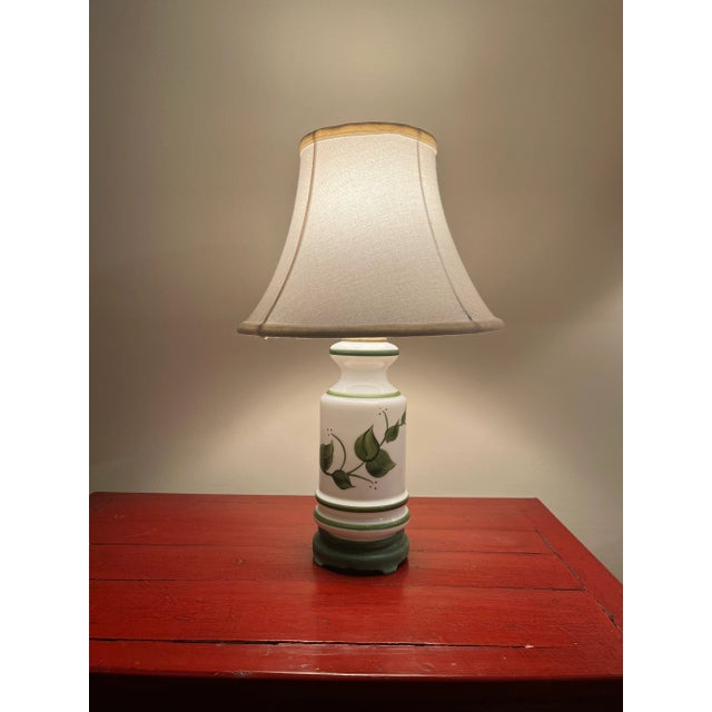 Vintage white milkglass table lamp with green handpainted leaves and a painted green wooden base. Has a one-way switch....