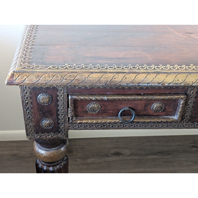 With gorgeous handcrafted brass accents and two drawers, this beautiful hand carved desk is in great condition for its age...
