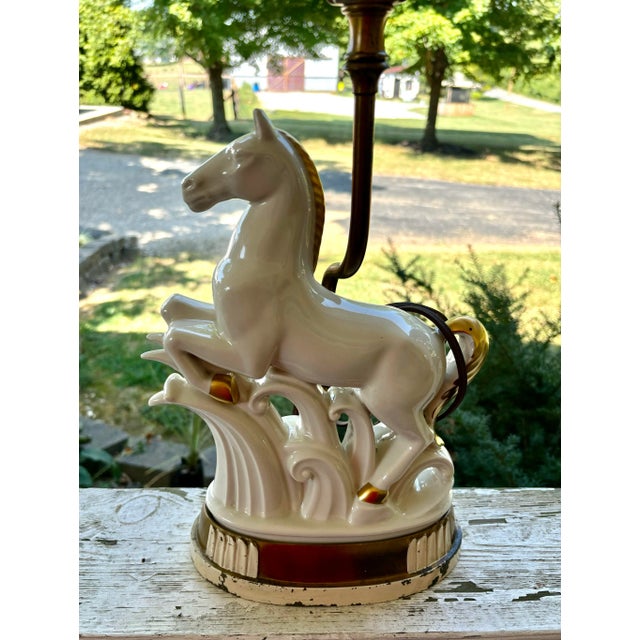 A striking vintage porcelain horse sculpture table lamp featuring a beautifully modeled leaping horse poised above a...