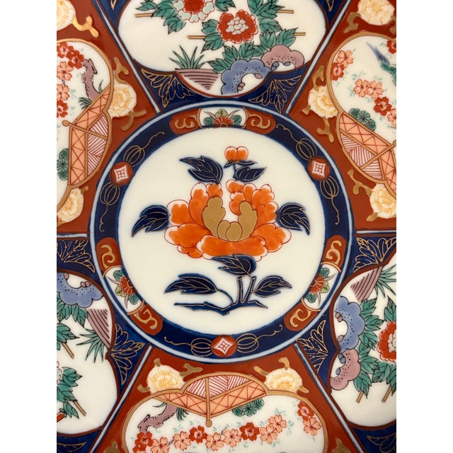 This vintage Imari style plate includes a center medallion featuring an orange and gold peony. The surrounding insets...