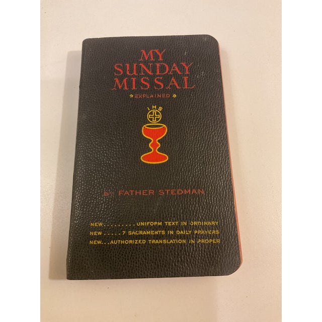 This compact Catholic missal features a black pebbled cover with red and gold lettering and traditional Eucharistic...