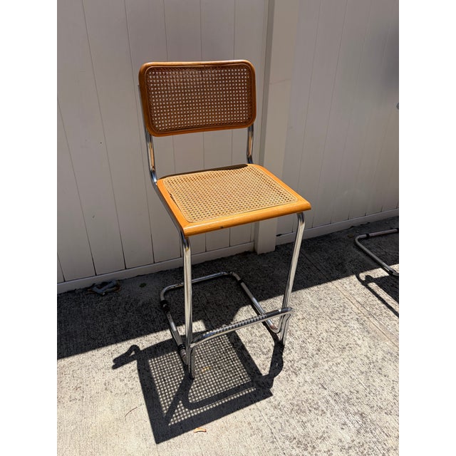 Striking vintage bar stool featuring a tubular chrome cantilever frame with warm-toned wood trim and woven cane panels on...