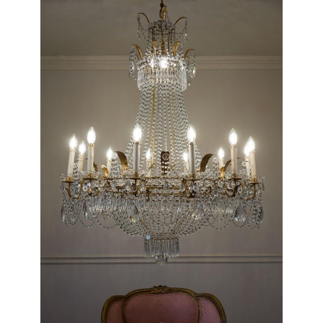 Large Empire-style chandelier in gilded iron with gold leaf, glass, and cut crystal, made in Italy in the 1940s. The...