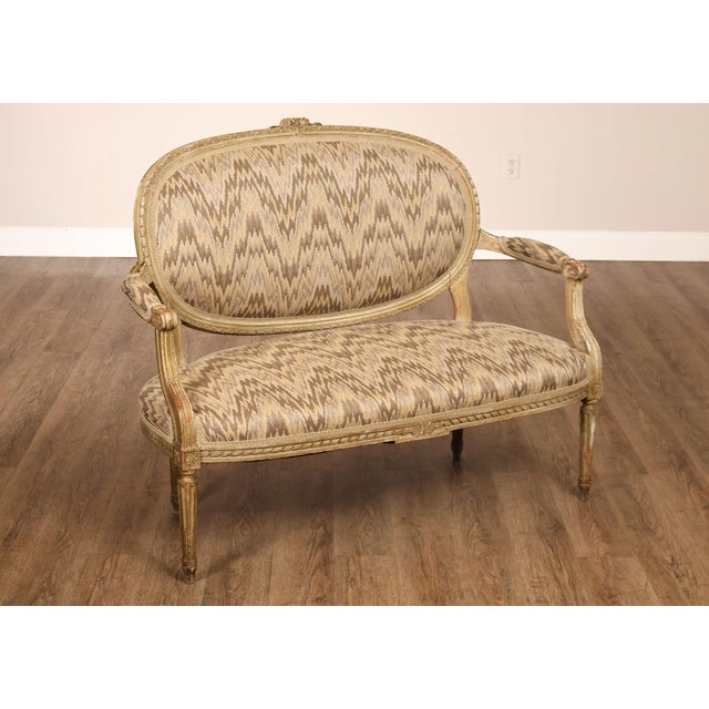 High Quality French Made Louis XVI Style Painted Settee. Features An Oval Upholstered Back, Carved Ribbon Crest, Fluted...