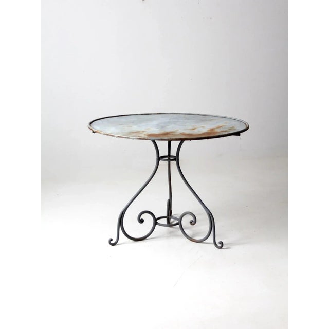 A charming antique metal garden table in a softly weathered blue-gray finish. The round tabletop is supported by...