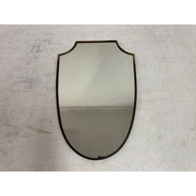 An Italian wall mirror from the 1950s, defined by its elegant shield-shaped silhouette and restrained use of line. The...
