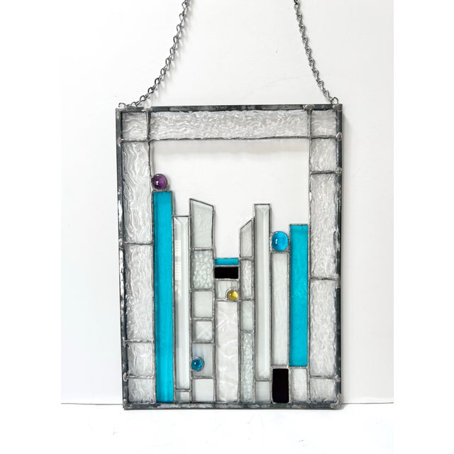 A vintage geometric stained glass panel combining saturated teal accents with textured clear glass and small jewel-tone...