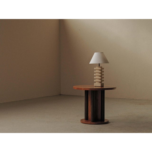 Round pedestal side table featuring a warm reddish-brown wood top and base, contrasted with a dark sculptural central...